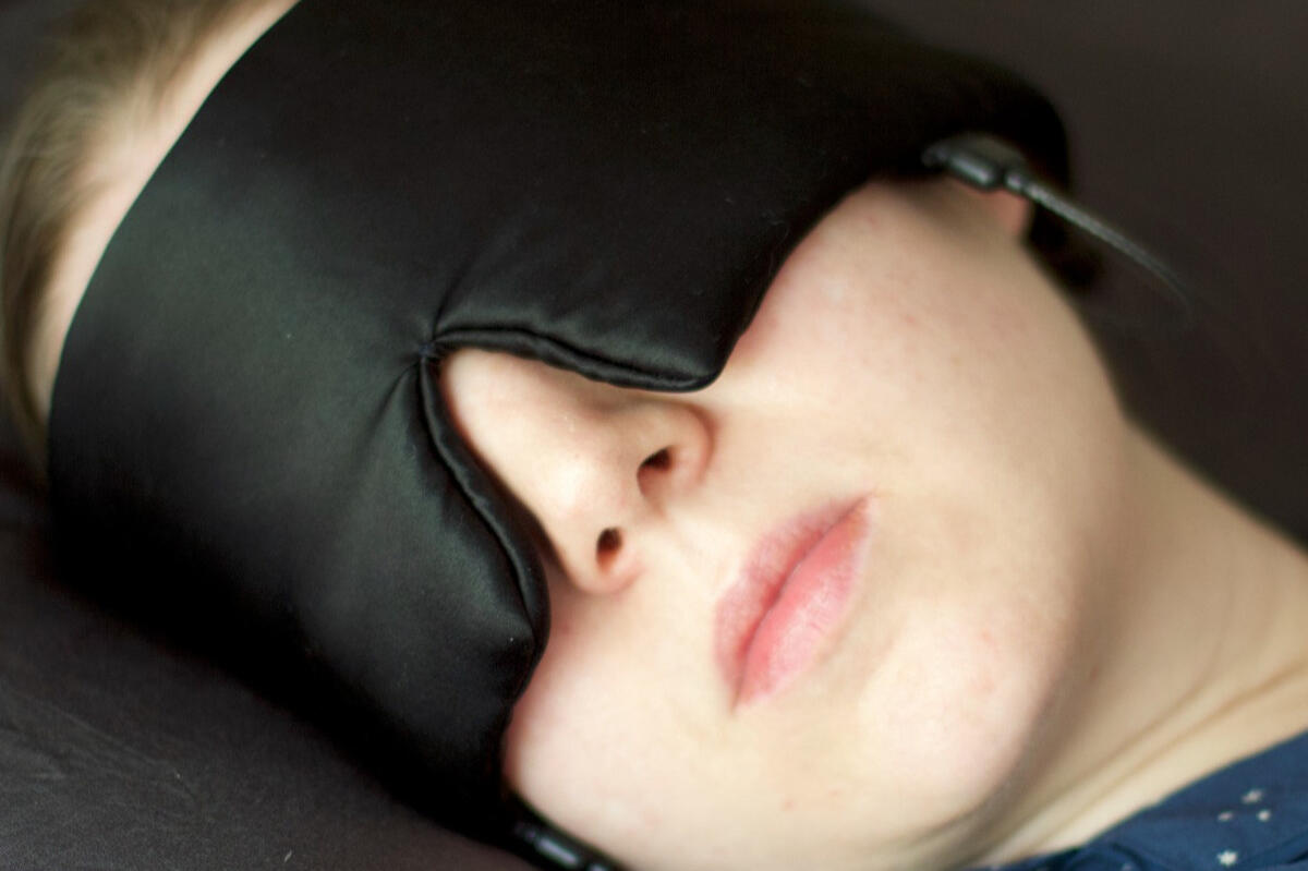Black sleep mask with two detachable short-lead earbuds and a separate control module.
